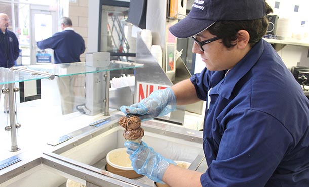 A Creamery employee scoops a cone of ice cream for a waiting customer