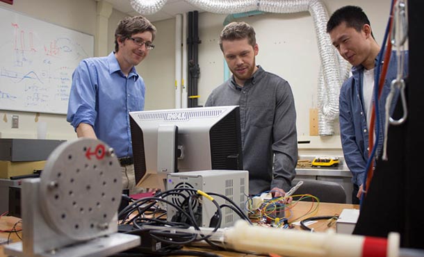 Jason Moore, David Pepley and Yichun Tang stand over the simulator training device